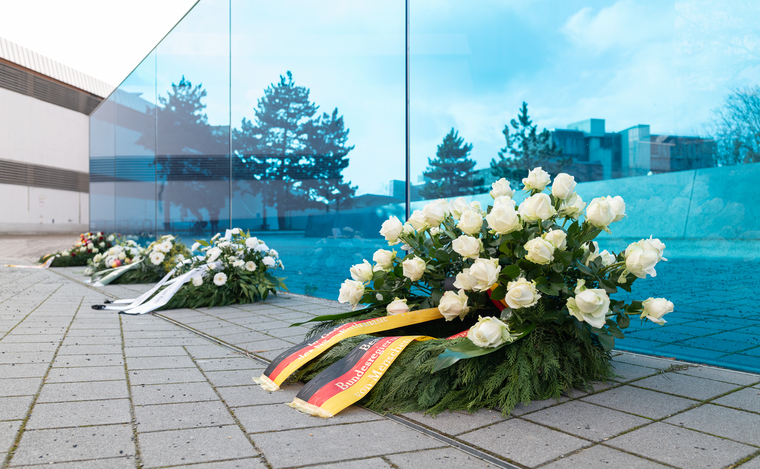 Vor einer blauen langen Glaswand liegen vier große Gedenkkränze mit Schleifen (Quelle: Behindertenbeauftragter/Konrad Schmidt) Vor einer blauen langen Glaswand liegen vier große Gedenkkränze mit Schleifen