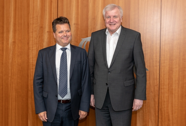 Die beiden Männer stehen nebeneinander vor einer Holzwand. Sie lächeln in die Kamera. (Quelle: BMI) Die beiden Männer stehen nebeneinander vor einer Holzwand. Sie lächeln in die Kamera.