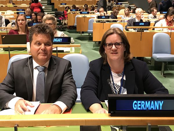 Jürgen Dusel und Kerstin Griese sitzen in einem Saal. Im Hintergrund sind weitere Delegationen aus anderen Ländern zu sehen, die ebenfalls sitzen. Im Vordergrund steht eine digitale Anzeige, auf der "Germany" (Deutschland) zu lesen ist. 