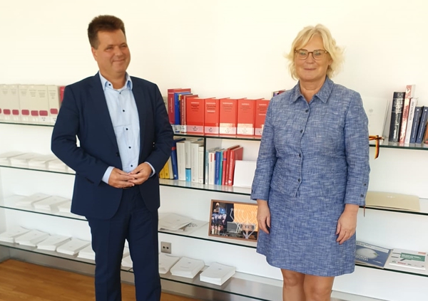 Jürgen Dusel (links) und Bundesministerin Christine Lambrecht (rechts) stehen vor einem Bücherregal und schauen in die Kamera