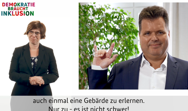 Standaufnahme des Videos: Rechts Jürgen Dusel, links die Gebärdensprachdolmetscherin, unten Untertitel