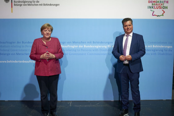 Jürgen Dusel und Bundeskanzlerin Dr. Angela Merkel. Die beiden stehen vor einer blauen Pressewand.